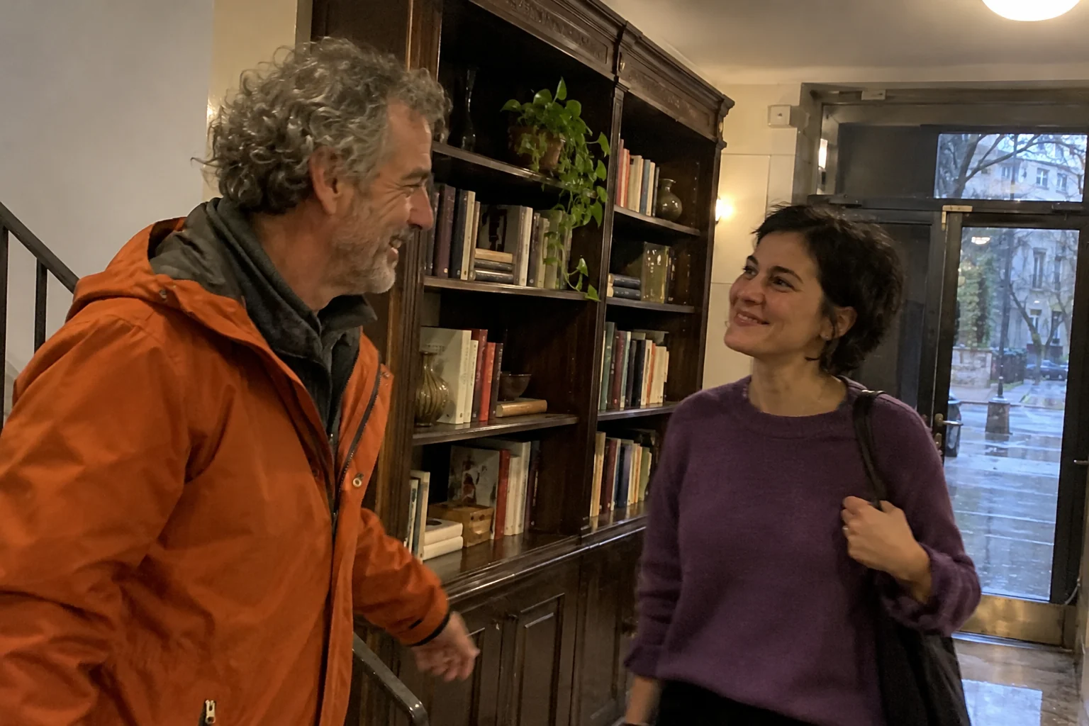 Dos vecinos se saludan junto a una biblioteca compartida de madera.